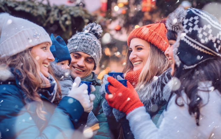 eine Gruppe von Freunden trinkt in der Kälte Glühwein auf einem Weihnachtsmarkt